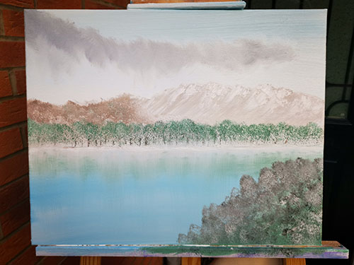 Winter lake with snow topped trees and distant mountains.